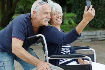 senior couple in wheelchair taking selfies outdoors
