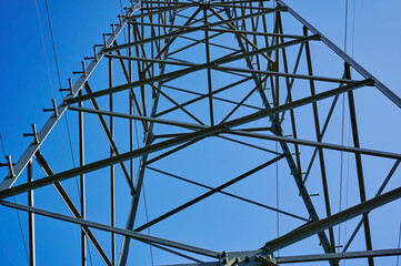 Low angle shot from below to the top of an electricity pylon against blue sky.