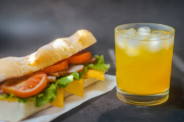 big tasty sandwich with tomato lettuce with soap and ham on the board. next to it is juice with ice in a glass.