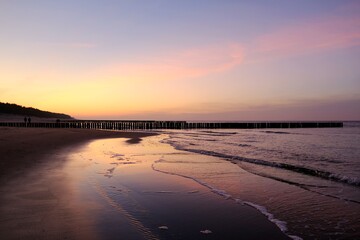 Beautiful sunset colors on the beach of sea and amazing reflection in water. Silhouette of breakwater on horizon.