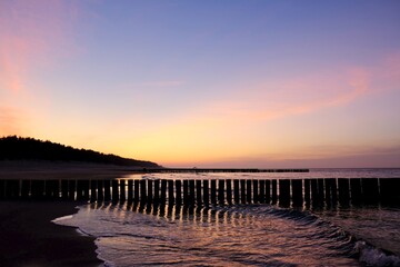 Obraz premium Beautiful sunset colors on the beach of sea. Silhouette of breakwater on foreground.