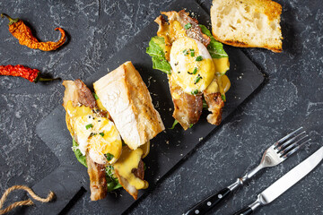 Sandwich with Eggs Benedict, bacon and salad on black stone background