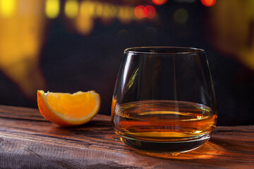 Glass of whiskey with orange slice on the wooden bar table on the background of bright yellow...