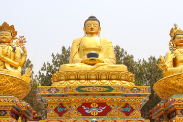 Three large gold colored Buddha statues sitting in Lotus position (Padmasana) in sunny day in Amideva Buddha Park (also known as Buddha Garden) located in the western part of Kathmandu city, Nepal.