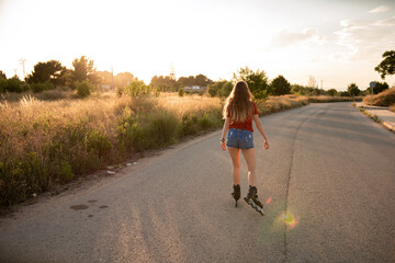 Fototapeta premium Chica rubia haciendo patinaje en línea por la carretera al atardecer durante el proceso de desescalada en España