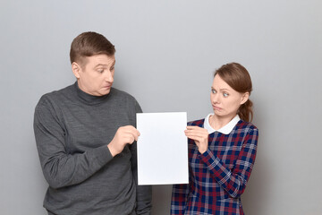 Portrait of adult couple holding together white blank paper sheet