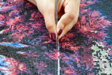 Girl collect diamond painting. Diamond embroidery with a tweezers. Acrylic rhinestones. Closeup,...