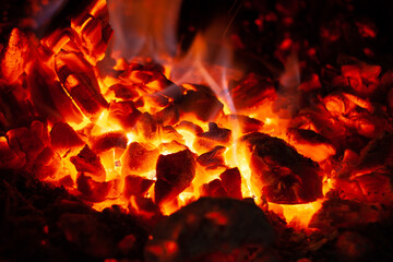 Glowing embers in hot red color, abstract background. The hot embers of burning wood log fire. Firewood burning on grill. Texture of fire fuel briquettes