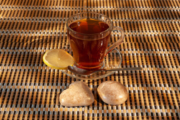 A cup with tea, lemon and pastries stands on a table covered with a mat.