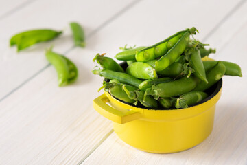 Fresh young green peas in pods in a yellow iron bowl, ripe organic vegetables