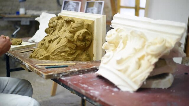 Sculptor create clay model of a Corinthian capitel with scrolls and unfurled acanthus leaves in restoration workshop