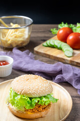 Crispy fried chicken burger on Round Wood plate served with french fries and ketchup on wooden background.