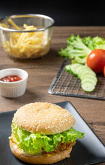 Crispy fried chicken burger on black plate served with french fries and ketchup on wooden background.