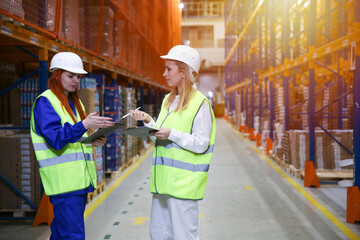 warehouse staff discuss warehouse processes. two women warehouse workers on the background of orange shelves with goods
