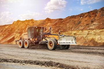 motor grader levels the ground on background of sandy quarry on the road construction  - obrazy, fototapety, plakaty