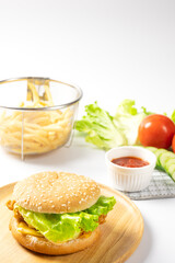 Crispy fried chicken burger on Round Wood plate served with french fries and ketchup on white background.