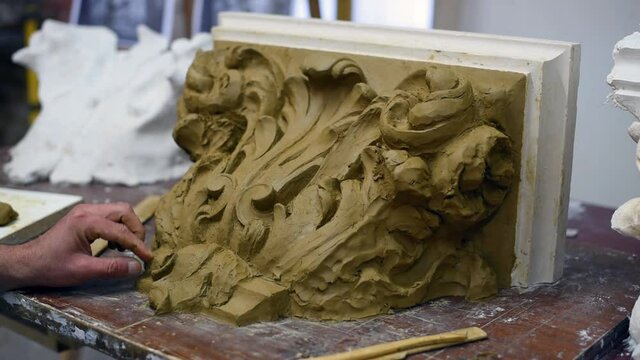 Sculptor create clay model of a Corinthian capitel with scrolls and unfurled acanthus leaves in restoration workshop
