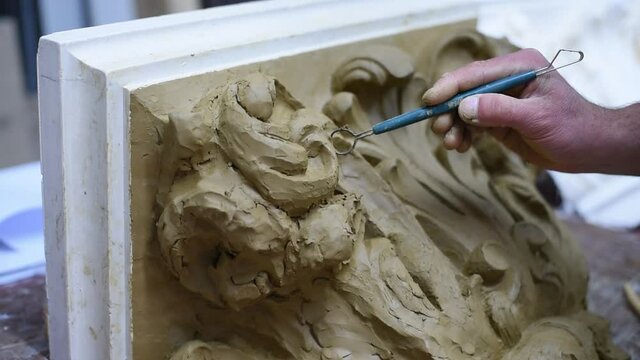 Sculptor create clay model of a Corinthian capitel with scrolls and unfurled acanthus leaves in restoration workshop