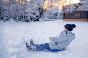 Fototapeta na wymiar Winter fun in the city. A boy rides on a slide of ice.