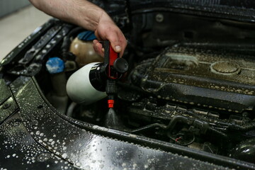 car engine washing close-up. car wash worker apply detergent on car engine. the mechanic's hand...