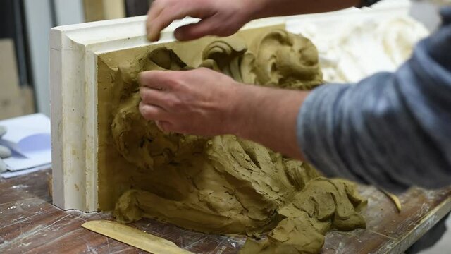 Sculptor create clay model of a Corinthian capitel with scrolls and unfurled acanthus leaves in restoration workshop