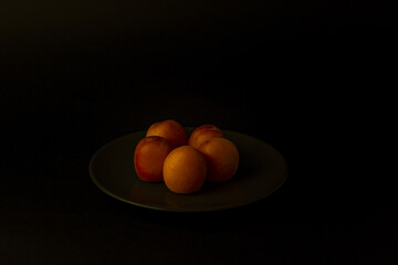  Still Life con albaricoque en un plato negro sobre fondo negro