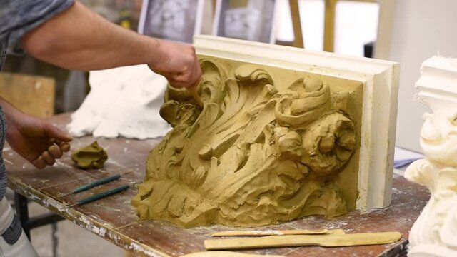 Sculptor create clay model of a Corinthian capitel with scrolls and unfurled acanthus leaves in restoration workshop