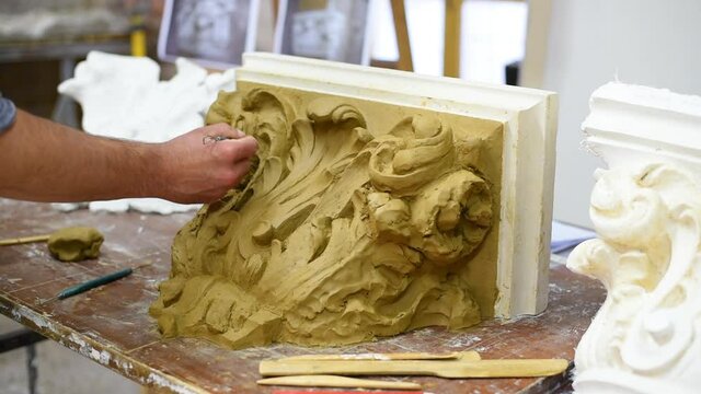 Sculptor create clay model of a Corinthian capitel with scrolls and unfurled acanthus leaves in restoration workshop