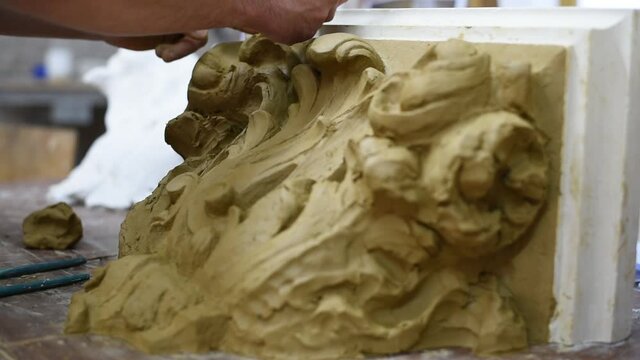 Sculptor create clay model of a Corinthian capitel with scrolls and unfurled acanthus leaves in restoration workshop