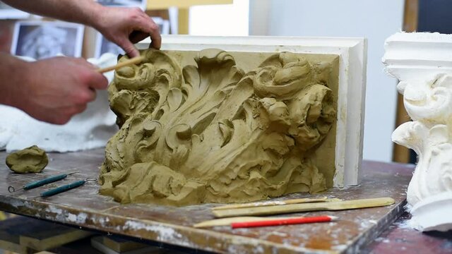 Sculptor create clay model of a Corinthian capitel with scrolls and unfurled acanthus leaves in restoration workshop