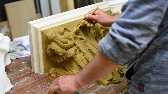 Sculptor create clay model of a Corinthian capitel with scrolls and unfurled acanthus leaves in restoration workshop