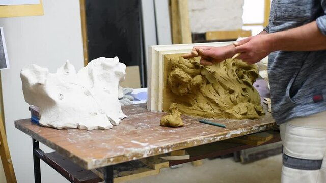 Sculptor create clay model of a Corinthian capitel with scrolls and unfurled acanthus leaves in restoration workshop