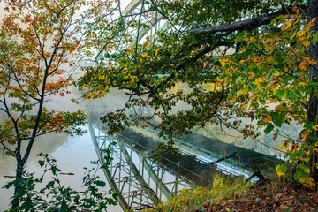 Route 9 Bridge over and reflected through trees and early morning fog in  Connecticut River  with colorful fall foliage, at Brattlebro, New Hampshire.