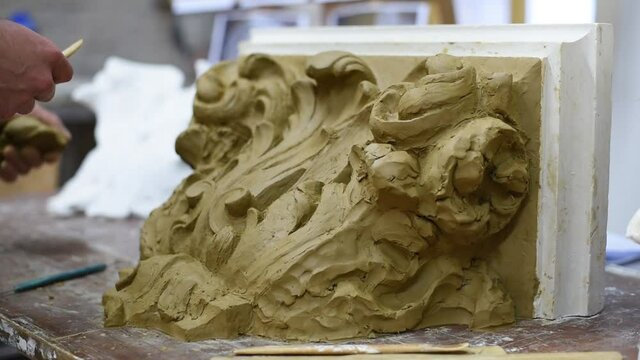 Sculptor create clay model of a Corinthian capitel with scrolls and unfurled acanthus leaves in restoration workshop