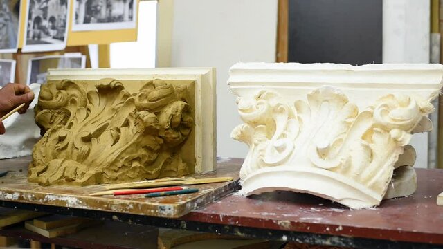 Sculptor create clay model of a Corinthian capitel with scrolls and unfurled acanthus leaves in restoration workshop