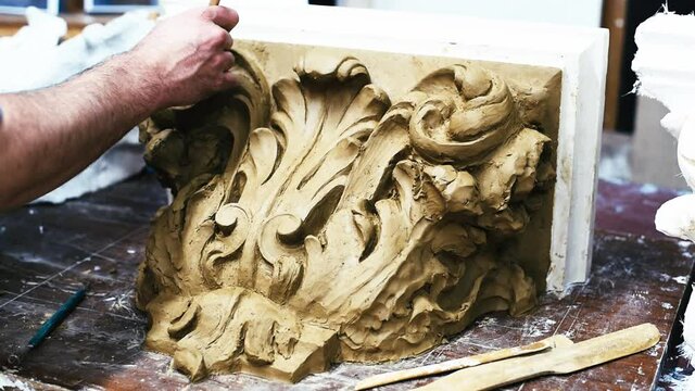 Sculptor create clay model of a Corinthian capitel with scrolls and unfurled acanthus leaves in restoration workshop