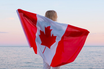 Achteraanzicht vrouw zwaaien nationale canada vlag buiten oceaan zee zonsondergang in de zomer - Canada dag, land, patriottisme, onafhankelijkheidsdag 1 juli