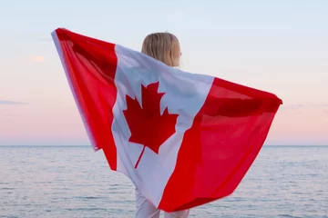 Zelfklevend Fotobehang Canada Achteraanzicht vrouw zwaaien nationale canada vlag buiten oceaan zee zonsondergang in de zomer - Canada dag, land, patriottisme, onafhankelijkheidsdag 1 juli