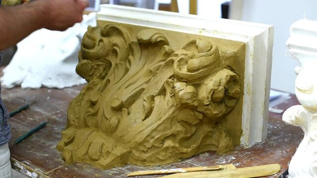 Sculptor create clay model of a Corinthian capitel with scrolls and unfurled acanthus leaves in restoration workshop