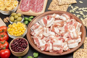 Bacon in ceramic plate. Cookies cheese corn olives tomatoes on table. Ingredients for english breakfast