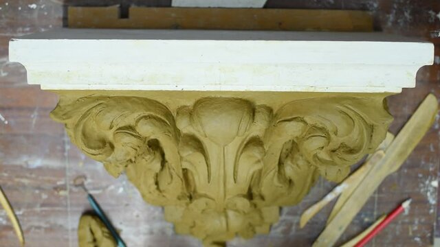 Sculptor create clay model of a Corinthian capitel with scrolls and unfurled acanthus leaves in restoration workshop