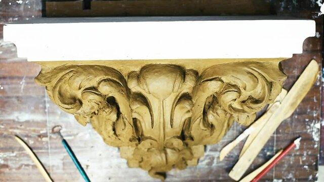 Sculptor create clay model of a Corinthian capitel with scrolls and unfurled acanthus leaves in restoration workshop