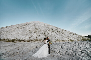 A handsome groom and young bride posing before the outdoor wedding ceremony with the mountains in the background.