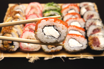 hand holds a roll with red fish of chopsticks, Sushi set on a background.