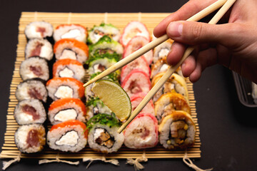 hand holds slice lime of chopsticks, Sushi set on background.