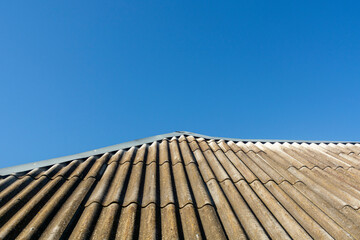 Old wavy slate roof against blue sky. Texture of old slate . Shed roof covered with old asbestos...