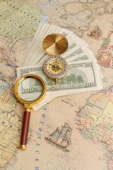 Fototapeta na wymiar A bundle of American dollars lies with a compass and a magnifying glass on the world map