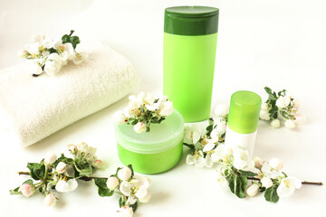Fototapeta na wymiar The concept of a good mood and a fresh morning : body care products and a white bath towel among Apple blossoms on a white background, side view.
