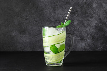 Detox cold water with sliced cucumber and mint leaves in glasses. Cucumber cocktail on dark background. Copy space