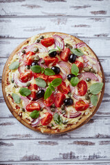 Tasty pizza with cherry tomatoes, cheese, black olives and fresh basil on wooden background. Top view.